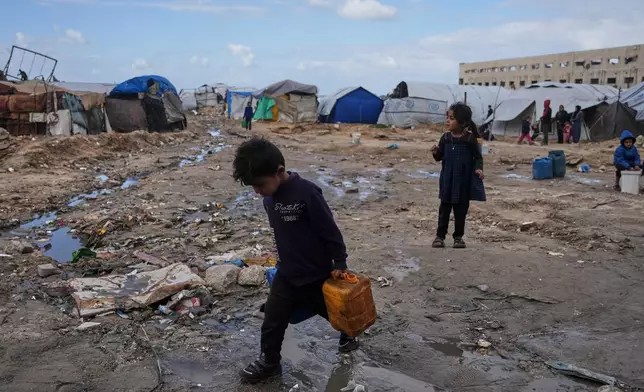 Palestinian children carry plastic jerrycans filled with water as they walk through a displacement camp in Gaza City, Sunday, Dec. 28, 2025. (AP Photo/Jehad Alshrafi)