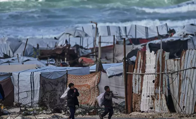 Palestinian children carry sacks filled with firewood as they walk through a displacement camp in Gaza City, Sunday, Dec. 28, 2025. (AP Photo/Jehad Alshrafi)