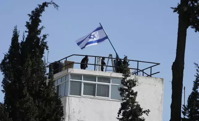 Israeli police and officials hang an Israeli flag on the compound of the United Nations agency for Palestinian refugees in East Jerusalem, after Israel police forcibly entered the compound, Monday, Dec. 8, 2025. (AP Photo/Mahmoud Illean)