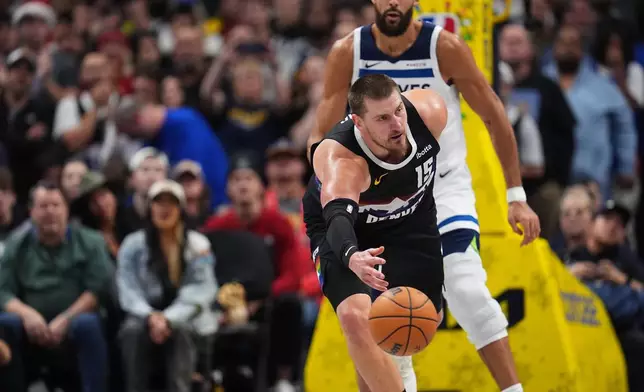 Denver Nuggets center Nikola Jokić, front, flips a loose ball as Minnesota Timberwolves center Rudy Gobert defends in overtime of an NBA basketball game Thursday, Dec. 25, 2025, in Denver. (AP Photo/David Zalubowski)