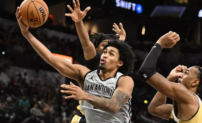 San Antonio Spurs guard Dylan Harper, front, drives for a layup as Washington Wizards guard Bilal Coulibaly, back, and center Alex Sarr, right, defend during the second half of an NBA basketball game in San Antonio, Thursday, Dec. 18, 2025. (AP Photo/Billy Calzada)