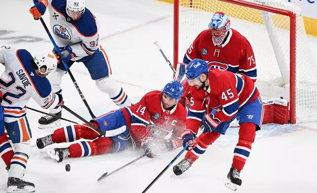 Montreal Canadiens goaltender Jakub Dobes (75) looks on as Canadiens' Nick Suzuki (14) blocks a shot by Edmonton Oilers' Matt Savoie (22) as Canadiens' Alexandre Carrier (45) and Oilers' Vasily Podkolzin (92) move in during the first period of an NHL hockey game, in Montreal, Sunday, Dec. 14, 2025. (Graham Hughes/The Canadian Press via AP)