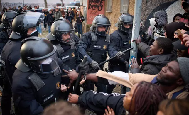 Migrants confront police as they begin carrying out eviction orders at an abandoned school building where hundreds of mostly undocumented migrants had been living, in Badalona, near Barcelona, Spain, Wednesday, Dec. 17, 2025. (AP Photo/Emilio Morenatti)