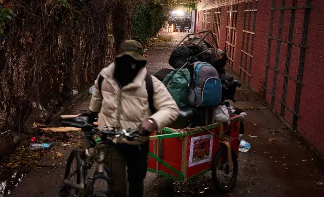 A migrant carries his belongings as police, in the background, prepares to carry out eviction orders at an abandoned school building where hundreds of mostly undocumented migrants had been living, in Badalona, near Barcelona, Spain, Wednesday, Dec. 17, 2025. (AP Photo/Emilio Morenatti)