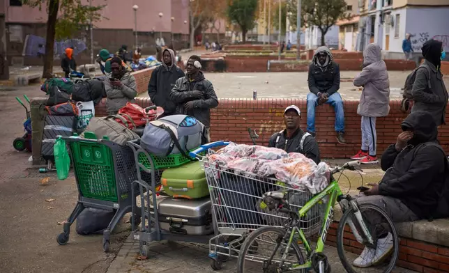Migrants sit together with their belongings after being evicted by police from an abandoned school where they had been living in Badalona, near Barcelona, Spain, Wednesday, Dec. 17, 2025. (AP Photo/Emilio Morenatti)