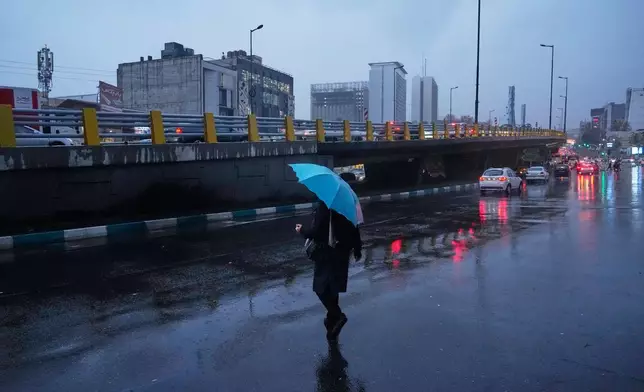 A woman holds an umbrella while crossing a street as rain falls in Tehran, Iran, Wednesday, Dec. 10, 2025. (AP Photo/Vahid Salemi)