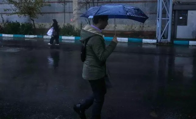 A man holds an umbrella while walking in bus station as rain falls in Tehran, Iran, Wednesday, Dec. 10, 2025. (AP Photo/Vahid Salemi)