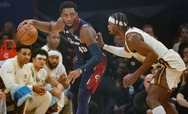 Cleveland Cavaliers' Donovan Mitchell (45) keeps the ball from Golden State Warriors' Buddy Hield, right, during the first half of an NBA basketball game in Cleveland, Saturday, Dec. 6, 2025. (AP Photo/Phil Long)