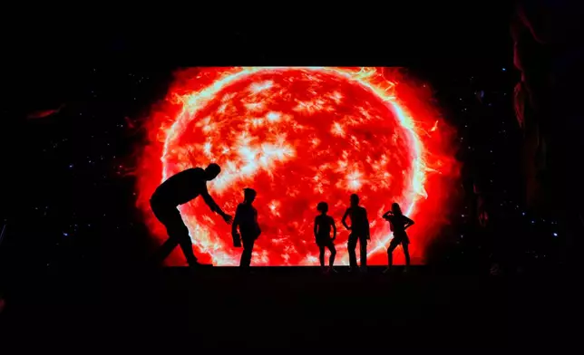 People pose for photos in front of a projection of the sun at an expo that focuses on the solar system in Caracas, Venezuela, Monday, Dec. 22, 2025. (AP Photo/Matias Delacroix)