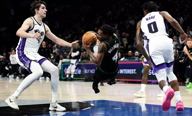 Minnesota Timberwolves guard Rob Dillingham, center, trips as he drives toward the basket while Sacramento Kings center Maxime Raynaud, left, and guard Malik Monk (0) defend during the first half of an NBA basketball game Sunday, Dec. 14, 2025, in Minneapolis. (AP Photo/Matt Krohn)
