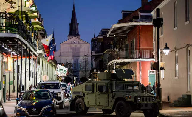 A man walking on Bourbon Street holds a flag reading "Love" as an armored vehicle sits parked on a street in the French Quarter as part of a National Guard deployment for New Year's celebrations in New Orleans, Tuesday, Dec. 30, 2025.