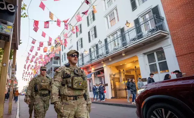 Walking under flags that memorialize victims of Jan. 1, 2025 attack, members of the Louisiana National Guard, military police, and Louisiana law enforcement agencies patrol the French Quarter along Bourbon Street and intersecting streets as part of a National Guard deployment for New Year's celebrations in New Orleans, Tuesday, Dec. 30, 2025. (AP Photo/Matthew Hinton)