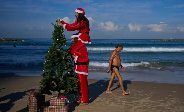 Surfers dressed as Santa Claus decorate a Christmas tree on the beach while filming a tourism advertisement ahead of Christmas, in Tel Aviv, Israel, Tuesday, Dec. 2, 2025. (AP Photo/Ohad Zwigenberg)