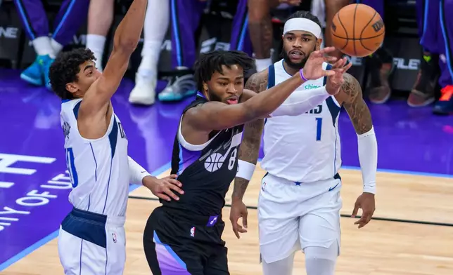 Utah Jazz guard Isaiah Collier, center, passes the ball while guarded by Dallas Mavericks guard Max Christie, left, during the first half of an NBA basketball game, Monday, Dec. 15, 2025, in Salt Lake City. (AP Photo/Tyler Tate)