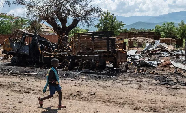 A boy walks past a burned-out vehicle as residents return to their homes in Luvungi, Democratic Republic of Congo, Saturday, Dec. 13, 2025. (AP Photo/Moses Sawasawa)