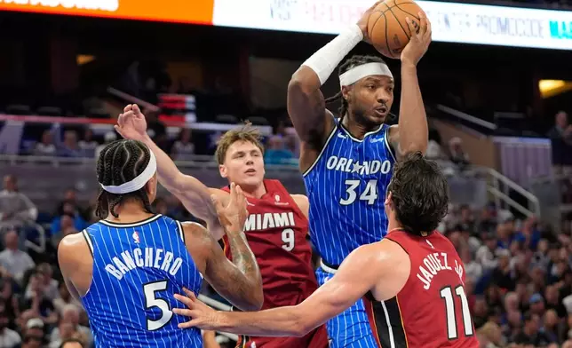 Orlando Magic center Wendell Carter Jr. (34) looks to pass the ball as he is caught between Miami Heat guard Pelle Larsson (9) and guard Jaime Jaquez Jr. (11) during the first half of an NBA basketball game, Friday, Dec. 5, 2025, in Orlando, Fla. (AP Photo/John Raoux)