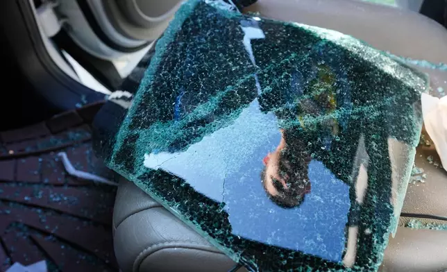 Jonathan Escalante stands over the broken window of his mother's car, which was shattered by federal immigration agents who took her away, during a federal immigration crackdown in Kenner, La., Tuesday, Dec. 9, 2025. (AP Photo/Gerald Herbert)