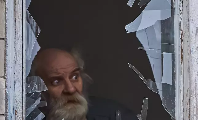 An elderly man looks out of his broken window as an apartment building was hit by a Russian drone during an aerial attack in Kyiv, Ukraine, Tuesday, Dec. 23, 2025. (AP Photo/Efrem Lukatsky)