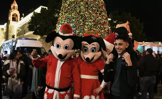 Palestinians pose for the pictures with performers in Manger Square in the West Bank city of Bethlehem, Friday, Dec. 12, 2025. (AP Photo/Mahmoud Illean)