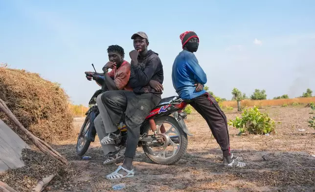 Issa Traore, left, Mamadou Camara, center, and Madassa Kebe, who moved from Mali to Senegal to pursue farming, sit on a scooter on a farm in Tambacounda, Senegal, Wednesday, Nov. 5, 2025. (AP Photo/Mark Banchereau)