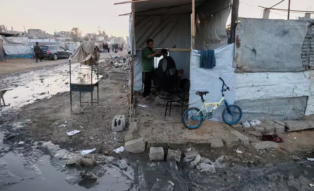 A barber cuts a man's hair inside a makeshift tented stall at a displacement camp in Jabalia, in the northern Gaza Strip, Sunday, Dec. 7, 2025. (AP Photo/Jehad Alshrafi)