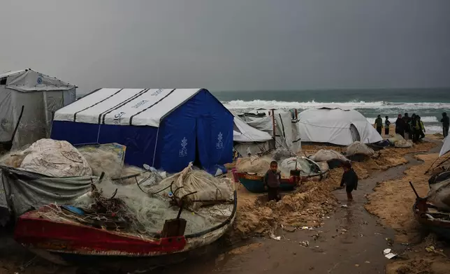 Displaced Palestinian children walk through a tent camp amid stormy weather on the beach in Khan Younis, Gaza Strip, Thursday, Dec. 11, 2025. (AP Photo/Abdel Kareem Hana)