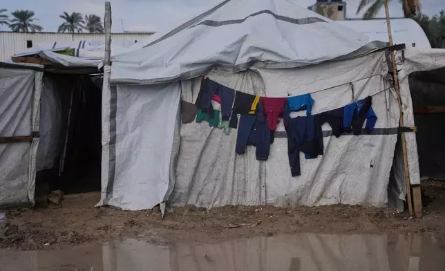 Clothes hang at the entrance of a tent next to flooded area in a temporary camp for displaced Palestinians after heavy rainfall in Deir al-Balah, central Gaza Strip, Friday, Dec. 12, 2025. (AP Photo/Abdel Kareem Hana)