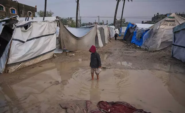 A Palestinian boy walks through an area in a temporary tent camp after heavy rainfall in Deir al-Balah, central Gaza Strip, Friday, Dec. 12, 2025. (AP Photo/Abdel Kareem Hana)