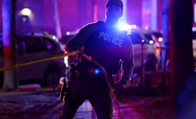 A police officer hangs yellow crime tape at Brown University in Providence, R.I., on Saturday, Dec. 13, 2025, during the investigation of a shooting. (AP Photo/Mark Stockwell)