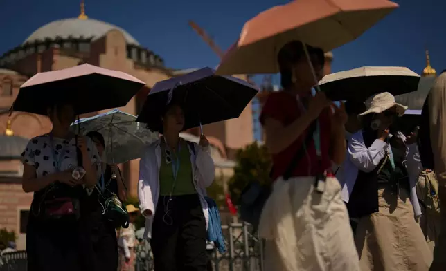 FILE - Tourists use umbrellas to shelter against the sun outside Hagia Sophia mosque during a hot summer day in Istanbul Aug. 12, 2025. (AP Photo/Francisco Seco, File)