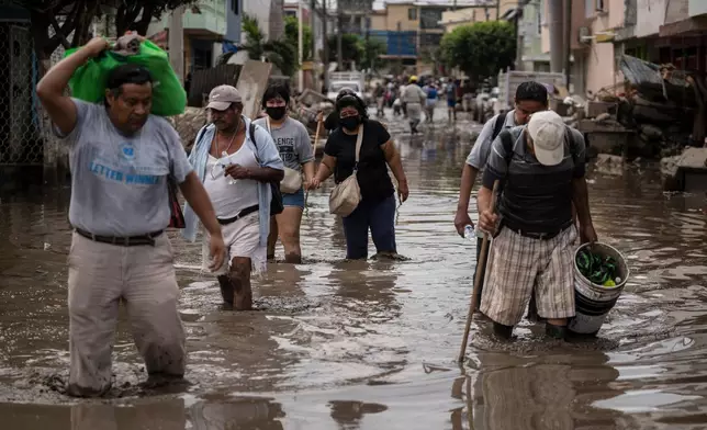 FILE - People traverse a flooded street in Poza Rica, Veracruz state, Mexico, Oct. 15, 2025, after torrential rain. (AP Photo/Felix Marquez, File)
