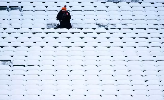 A fan sits in the stadium seats covered in snow before an NFL football game between the Cincinnati Bengals and the Baltimore Ravens, Sunday, Dec. 14, 2025, in Cincinnati. (AP Photo/Carolyn Kaster)