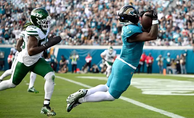 Jacksonville Jaguars running back Travis Etienne Jr. (1) makes a catch for a touchdown against New York Jets linebacker Quincy Williams (56) during the first half of an NFL football game, Sunday, Dec. 14, 2025, in Jacksonville, Fla. (AP Photo/Phelan M. Ebenhack)