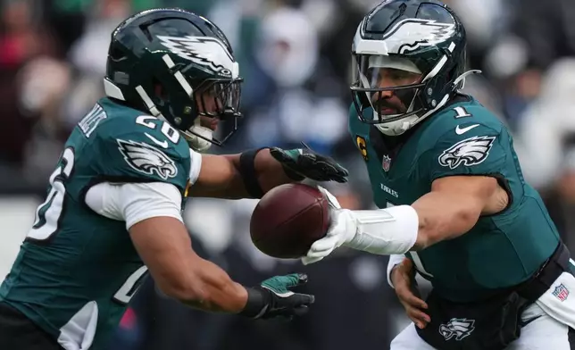 Philadelphia Eagles quarterback Jalen Hurts (1) hands off the ball to Philadelphia Eagles running back Saquon Barkley, left, during the first half of an NFL football game against the Las Vegas Raiders on Sunday, Dec. 14, 2025, in Philadelphia. (AP Photo/Matt Slocum)