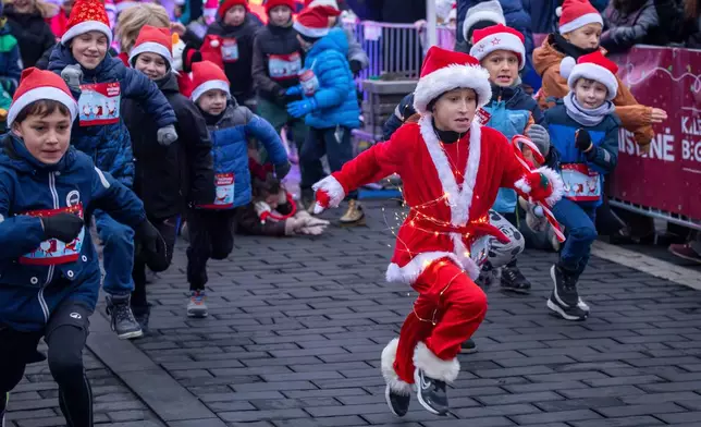 Decked in a Santa outfit and holiday lights, a child bolts from the starting line of the annual Christmas run in Vilnius, Lithuania, Saturday, Dec. 6, 2025. (AP Photo/Mindaugas Kulbis)