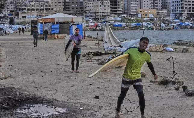 Palestinian Khalil Abu Jayyab, front, and Tahseen Abu Assi carry their surfing boards as they enter the water along a damaged shoreline in Gaza City, Sunday, Dec. 28, 2025. (AP Photo/Jehad Alshrafi)