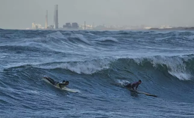 Palestinian Khalil Abu Jayyab, right, and Tahseen Abu Assi surf on the beach of Gaza City, Sunday, Dec. 28, 2025. (AP Photo/Jehad Alshrafi)