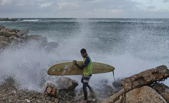 Palestinian Khalil Abu Jayyab carries his surfing board as they enter the water along a damaged shoreline in Gaza City, Sunday, Dec. 28, 2025. (AP Photo/Jehad Alshrafi)