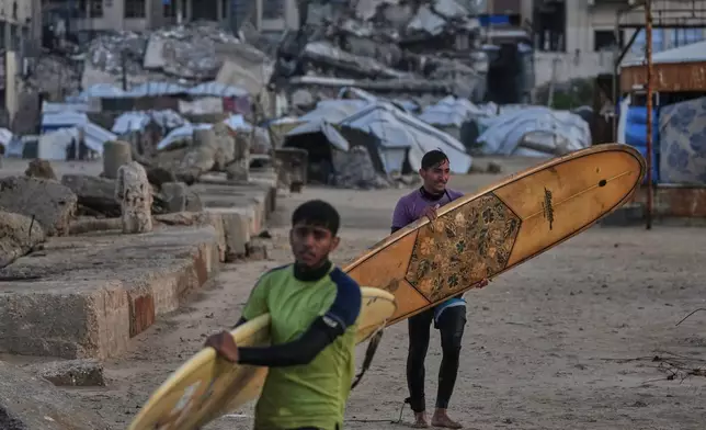Palestinian Khalil Abu Jayyab, front, and Tahseen Abu Assi carry their surfing boards as they enter the water along a damaged shoreline in Gaza City, Sunday, Dec. 28, 2025. (AP Photo/Jehad Alshrafi)