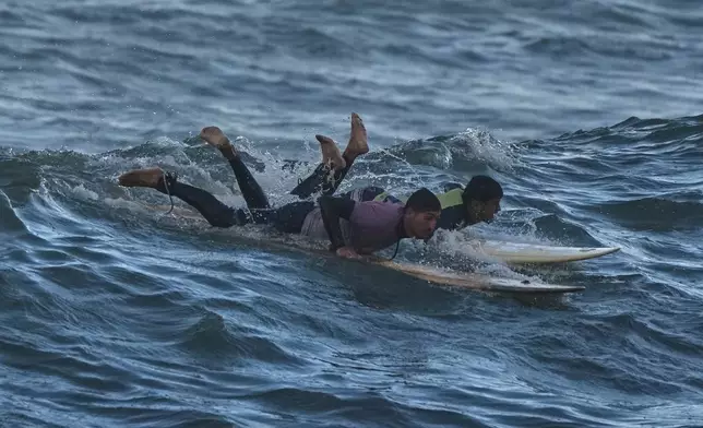 Palestinian Khalil Abu Jayyab, right, and Tahseen Abu Assi surf on the beach of Gaza City, Sunday, Dec. 28, 2025. (AP Photo/Jehad Alshrafi)
