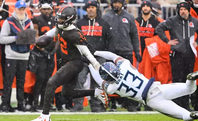 Cleveland Browns quarterback Shedeur Sanders (12) escapes a tackle attempt by Tennessee Titans' Cedric Gray (33) in the first half of an NFL football game in Cleveland, Sunday, Dec. 7, 2025. (AP Photo/David Richard)