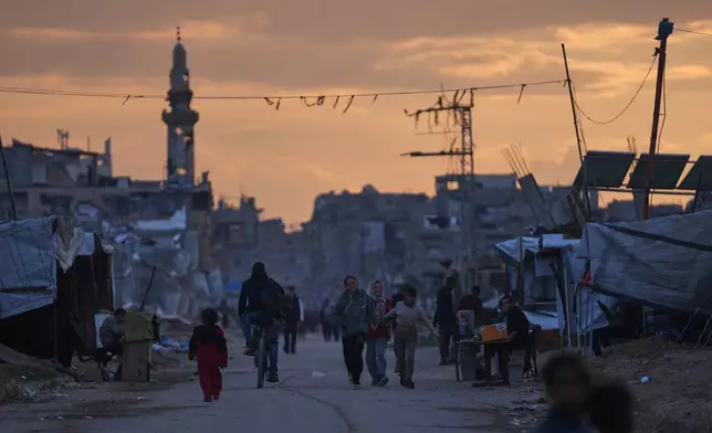 Palestinian youth walk along a tent camp for displaced people as the sun sets in Nuseirat, central Gaza Strip, Friday, Dec. 26, 2025. (AP Photo/Abdel Kareem Hana)