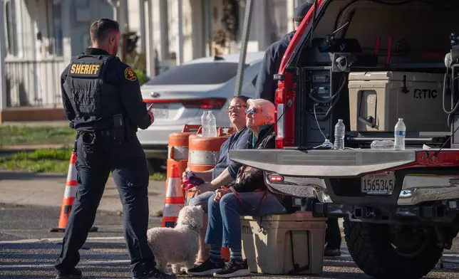 A police officer talks with residents effected from the gas explosion on the 800 block of East Lewelling Boulevard, Thursday, Dec. 11, 2025, in Hayward, Calif. (AP Photo/Minh Connors)