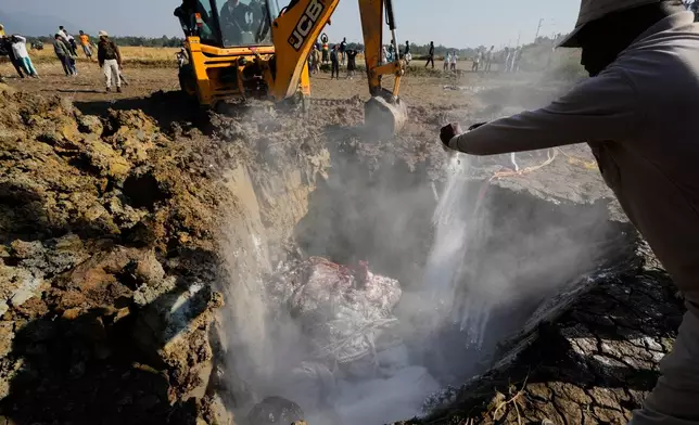 Forest officials spray salt to decompose the carcass of an Asiatic wild elephant burying in a pit after a speeding train hit a heard of wild elephant in the early morning in Changjurai village east of Guwahati, India, Saturday, Dec. 20, 2025. (AP Photo/Anupam Nath)