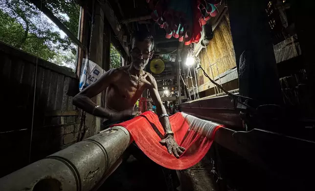 A weaver looks at the design blueprint for a Tangail saree as he operates a loom at a weaving workshop in Tangail District, Bangladesh, Nov. 5, 2025. (AP Photo/Mahmud Hossain Opu)
