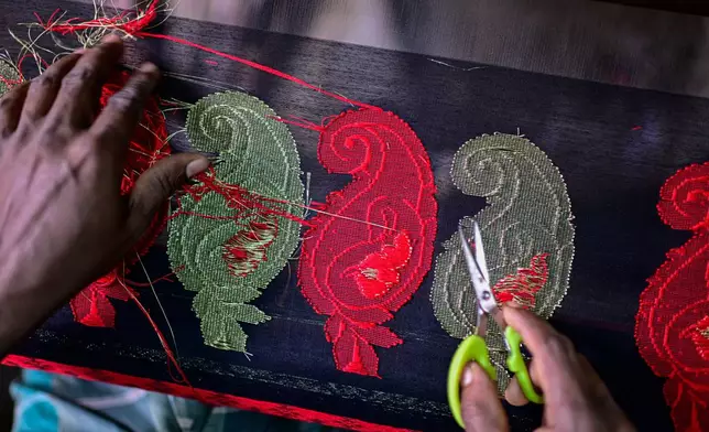 An artisan cuts excess thread from a Tangail saree at a weaving workshop in Tangail District, Bangladesh, Nov. 5, 2025. (AP Photo/Mahmud Hossain Opu)
