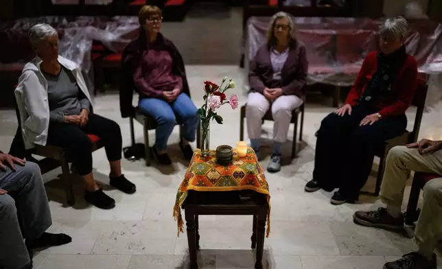 People sit around a table with an orange tapestry gifted by Himalayan refugees, an incense bowl, flowers and a candle during an interfaith meditation practice at All Saints Episcopal Church in Pasadena, Calif., on Monday, Dec. 15, 2025. (AP Photo/William Liang)