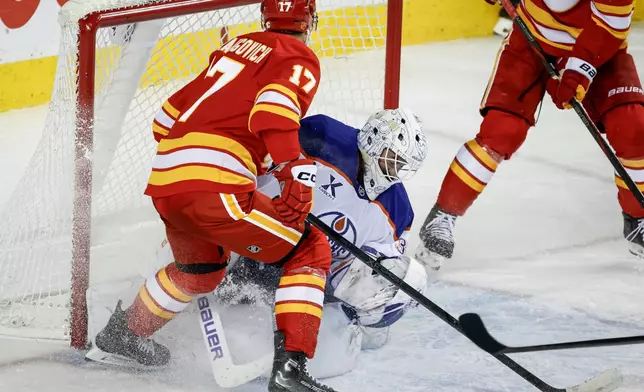 Edmonton Oilers goalie Connor Ingram, centeer, is knocked over by Calgary Flames' Yegor Sharangovich (17) during the third period of an NHL hockey game in Calgary, Alberta, Saturday, Dec. 27, 2025. (Jeff McIntosh/The Canadian Press via AP)
