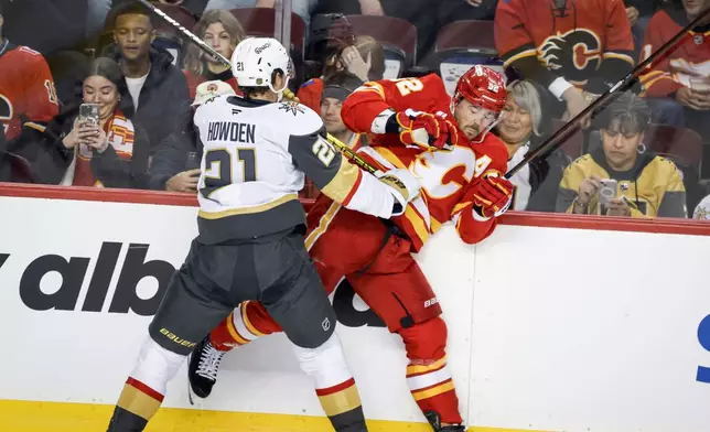 Vegas Golden Knights' Brett Howden, left, checks Calgary Flames' MacKenzie Weegar, right, during first-period NHL hockey game action in Calgary, Saturday, Dec. 20, 2025. (Jeff McIntosh/The Canadian Press via AP)