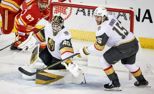 Vegas Golden Knights goalie Akira Schmid, center, and Noah Hanifin (15) reach for the puck as Calgary Flames' Matt Coronato (27) looks on during second-period NHL hockey game action in Calgary, Saturday, Dec. 20, 2025. (Jeff McIntosh/The Canadian Press via AP)